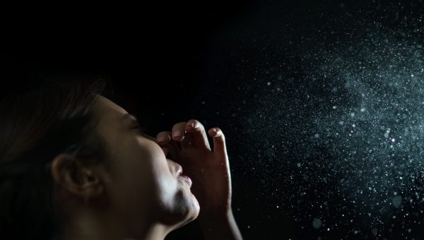 Woman sneezes into the air. All of the droplets forming into aerosols can be seen.